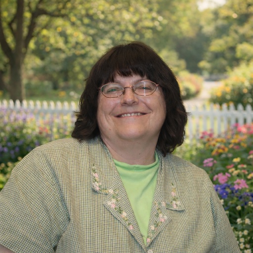 woman outside in front of a fenced flower garden